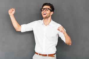 Happy winner. Cheerful young man gesturing and keeping his mouth open while standing against grey background photo
