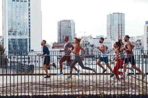 toda la longitud de los jóvenes con ropa deportiva trotando mientras hacen ejercicio en el puente al aire libre foto