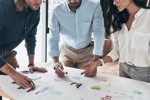 desarrollando una nueva estrategia. primer plano de jóvenes empresarios confiados que se comunican juntos mientras trabajan con planos en la oficina foto