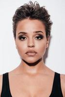 Portrait of beauty. Portrait of beautiful young short hair woman in black tank top looking at camera while standing against white background photo