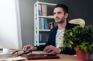 Concentrated on work. Concentrated young man working on computer while sitting at his working place in office photo