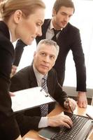 Discussing a report. Three business people in formalwear discussing something and looking at laptop photo