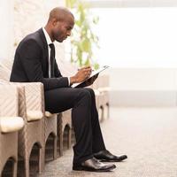 Making notes. Side view of confident young African businessman writing something in his note pad while sitting on the chair photo