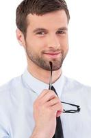 Just inspired. Portrait of handsome young man in formalwear holding glasses and looking at camera while standing isolated on white background photo