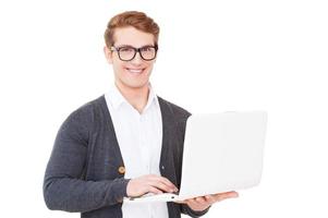 trabajando en la computadora portátil. un joven apuesto que trabaja en una laptop y sonríe mientras está aislado en blanco foto