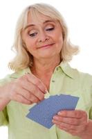 Senior lady playing cards. Cheerful senior woman holding playing cards and smiling while standing isolated on white background photo