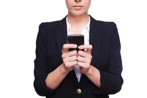 escribiendo un mensaje de negocios. primer plano de mujer joven en ropa formal sosteniendo teléfono móvil mientras está de pie aislado en blanco foto