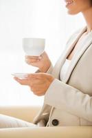 Coffee break. Side view of thoughtful young businesswoman in suit drinking coffee and looking away while sitting at the chair photo