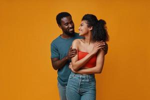 hermosa joven pareja africana sonriendo y abrazándose mientras está de pie contra el fondo amarillo foto