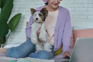 Teenage girl using laptop while sitting on bed with her dog photo