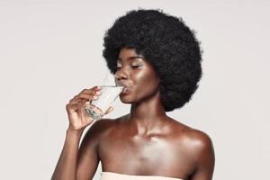 Portrait of beautiful young African woman drinking water while standing against gray background photo