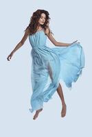 Levitation. Full length studio shot of attractive young woman in elegant dress hovering against grey background photo