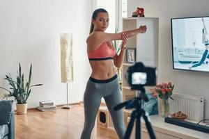 atractiva mujer joven con ropa deportiva haciendo ejercicio y sonriendo mientras hace videos en las redes sociales foto