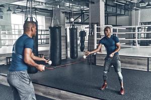 Another way of training. Handsome young African man in sport clothing exercising using balls while standing in front of the mirror in the gym photo