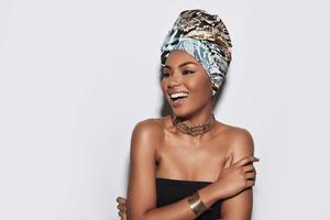Picture of a goddess. Attractive young African woman in turban smiling while standing against grey background photo