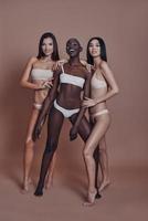Feeling free. Full length of three attractive mixed race women looking at camera and smiling while standing against brown background photo
