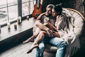 Romantic couple. Top view of beautiful young loving couple embracing and looking through window while sitting in big cozy chair at home photo