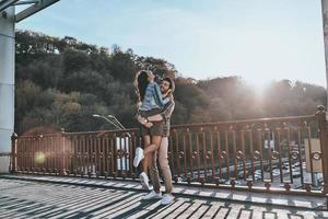 tan genial estar enamorado de un hombre guapo que lleva a una mujer joven y atractiva mientras está de pie en el puente al aire libre foto
