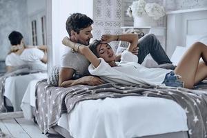 sentirse seguro y protegido cerca de él. hermosa pareja joven descansando y sonriendo mientras está acostado en la cama en casa foto