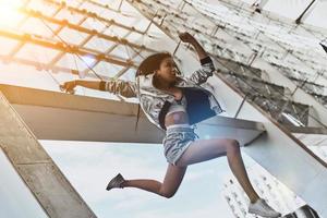 Full of energy. Attractive young woman in casual wear looking straight while jumping outdoors photo