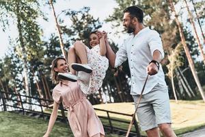 Playing together. Mother and father swinging daughter and smiling while walking in the park photo
