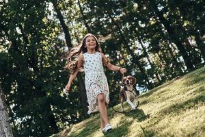 Full length of cute little girl playing with her dog and smiling while running outdoors photo