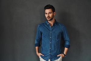Confident and handsome. Handsome young man in denim shirt looking at camera and smiling while standing against grey background photo