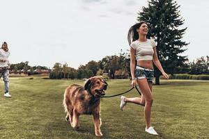 Carefree and happy.  Full length of beautiful young woman running with dog while her boyfriend running behind photo