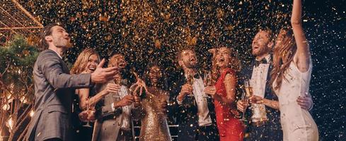 Group of happy people in formalwear having fun together with confetti flying all around photo