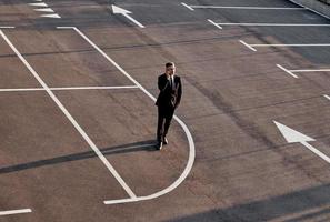 Top view of man in formalwear talking on mobile phone while standing on parking lot with arrow sign on it photo