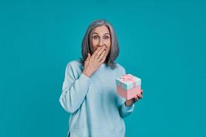 Mature beautiful woman holding gift box and covering mouth with hand photo