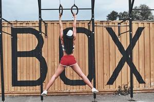 Suspension training. Full length rear view of young woman in sports uniform exercising outdoors photo