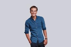 Young and carefree. Handsome young man looking away and smiling while standing against grey background photo