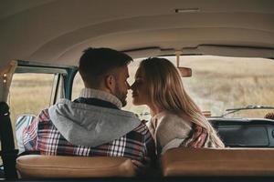 Lucky to have each other. Beautiful young couple smiling while sitting face to face on the front passenger seats in retro style mini van photo