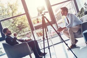 Creating interesting content. Two young men in smart casual wear talking while making new video indoors photo