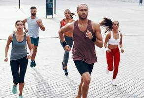 Group of young people in sports clothing jogging while exercising on the sidewalk outdoors photo