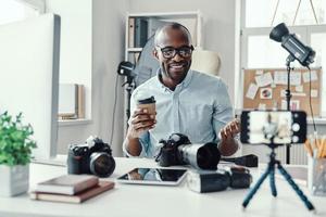 Handsome young African man in shirt smiling and telling something while making social media video photo