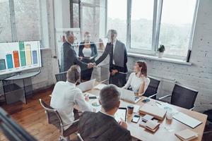 vista superior de los empresarios modernos dándose la mano mientras trabajan junto con su equipo en la sala de juntas foto