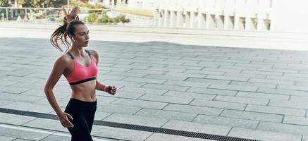 Beautiful young woman in sports clothing running outdoors photo