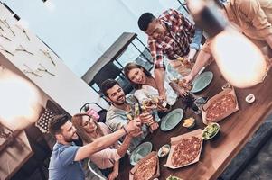 Top view of young people in casual wear gesturing and smiling while having a dinner party indoors photo