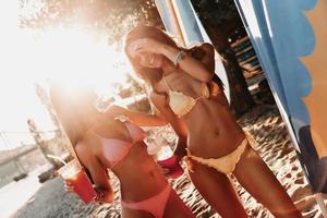 gran tiempo juntos. dos atractivas mujeres jóvenes sonriendo y disfrutando de cócteles mientras se divierten en la playa foto