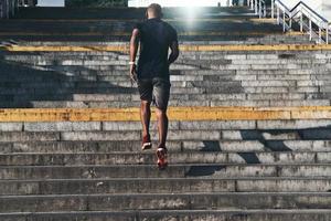 Healthy habits. Full length rear view of young African man in sports clothing running up the stairs while exercising outdoors photo