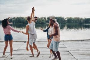 deja que la fiesta comience toda la longitud de los jóvenes con ropa informal sonriendo y gesticulando mientras disfrutan de la fiesta en la playa foto