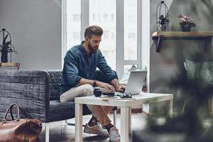 Working hard to achieve success. Thoughtful young modern man using computer while sitting at his working place photo