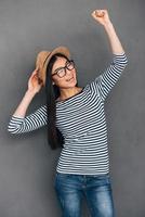 Pure joy. Beautiful young Asian woman in hat gesturing and looking happy while standing against grey background photo