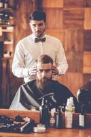 Looking perfect. Hairdresser checking symmetry of haircut of his client at barbershop photo