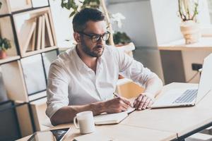 Concentrated at work. Confident mature man writing something in note pad while sitting at his working place in office photo