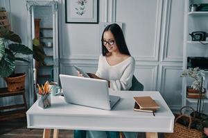 gran idea hermosa mujer joven sonriendo y trabajando usando una tableta digital mientras está sentada en la oficina en casa foto