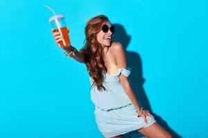 Party girl. Attractive young woman smiling and toasting you while standing against blue background photo