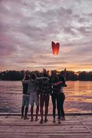 Flying away. Full length rear view of young people embracing and gesturing while looking at floating sky lantern photo